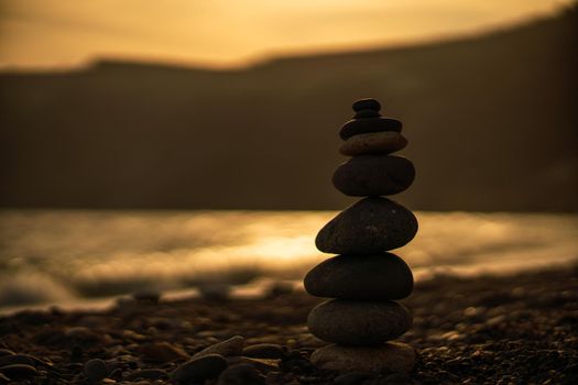 Pebble pyramid silhouette on the beach. Sunset with sea in the background. Zen stones on the sea beach concept, tranquility, balance. Selective focus