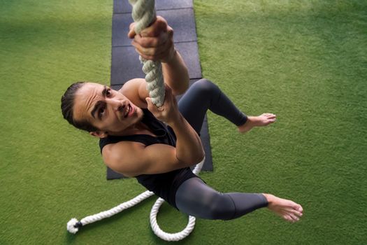 young man strength training by climbing a rope
