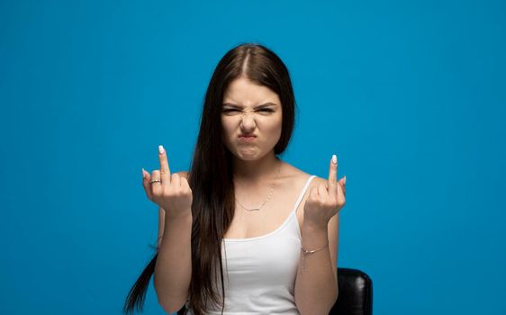 Portrait of rude vulgar woman showing middle fingers, impolite gesture of disrespect, looking with aggression hate on blue background.