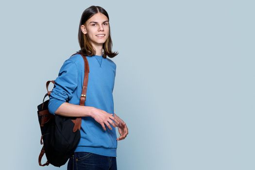 Portrait of young guy with backpack on gray background, copy space