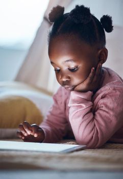 I wonder what Ill read today. a little girl using her digital tablet in her bedroom.