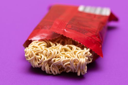 Opened Package with Uncooked Instant Noodles on Violet Background