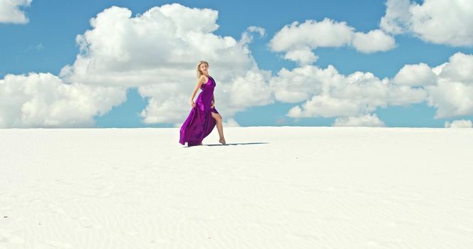 Cinematic slow motion of a woman walking on a sand dune. Barefoot woman traveler in a dress swinging in the wind on the undulating surface of the sandy desert with a cloud in the background. 4K Scenic nature