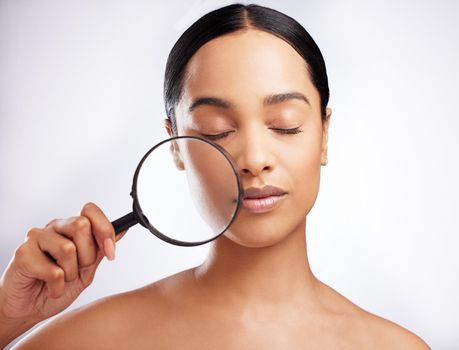 Take a look at her magnificent and flawless skin. Studio shot of a beautiful young woman holding a magnifying glass to her face against a white background.