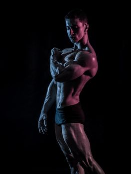 Handsome bodybuilder doing classic double biceps pose, looking away, on dark background