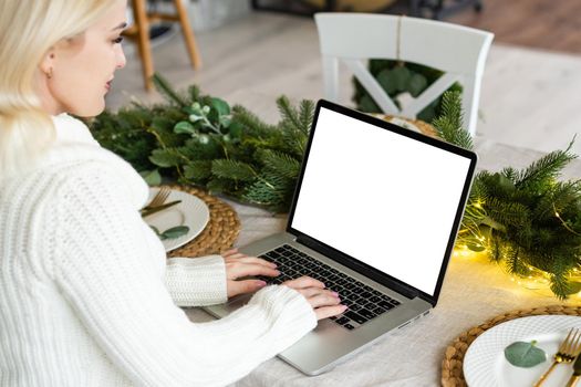 Young woman work on laptop with blank display screen with mockup copy space. Modern home living room interior design. Work at home concept. christmas
