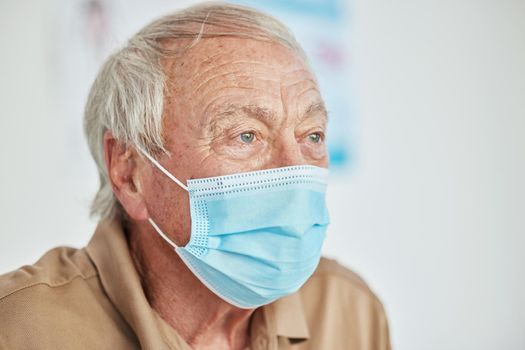 I really need to think about this. a senior man sitting alone and wearing a face mask in the clinic during his consult.