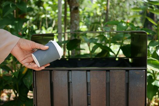 women hand throwing an empty paper coffee cup in the garbage trash or bin
