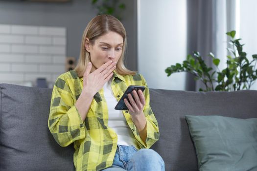 Woman alone at home, frustrated and shocked looking at the phone screen