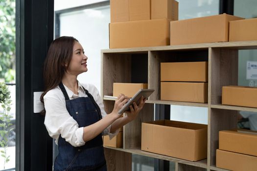 Asian female entrepreneur checking orders to arrange the produce before packing the products in the inner boxes with the customers. Freelance concepts