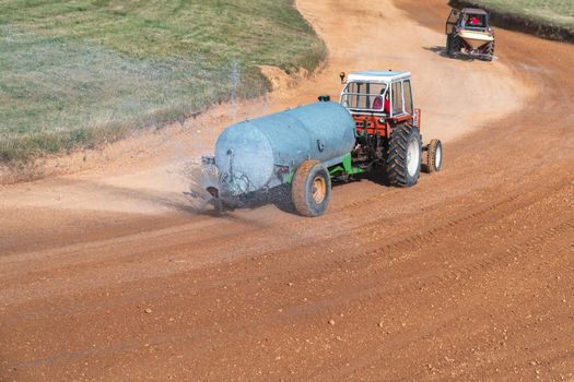 a tractor with a tank sprinkles water on the autocross track before the races