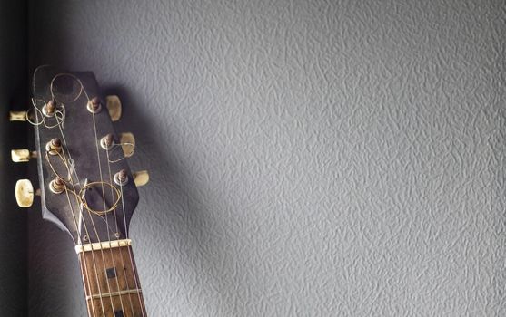 An acoustic old guitar in dust stands against a gray wall with copy space. Background for a screensaver with a musical instrument in the old style.