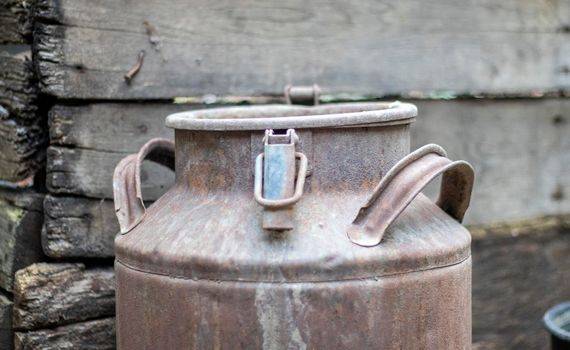 One old rusty metal can in the countryside. Container for transporting liquids, milk or liquid fuels with multiple handles. Milk bank of a cylindrical form with a wide mouth. Bottle with sealed cap.