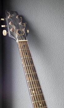 An acoustic old guitar in dust stands against a gray wall with copy space. Background for a screensaver with a musical instrument in the old style. Vertical photography.