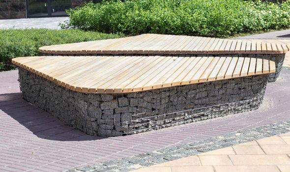 Wooden benches from gabion baskets with stones inside. Wood mounted on gabions. Benches of modern design. There is a recreation area. Detail of a low gabion wall with a wooden top.