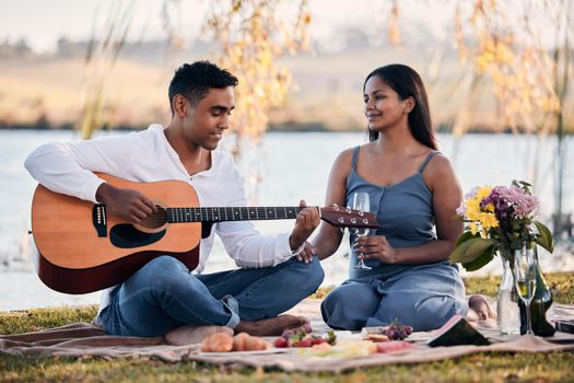 Life is a song, love is the music. a young man playing a guitar while on a picnic with his girlfriend at a lakeside.