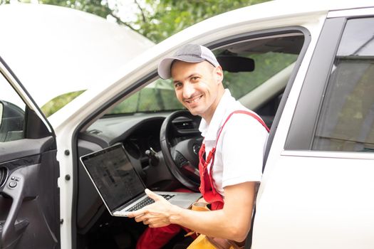 Mechanic with laptop near car engine. Modern car diagnostic program on screen. Car service concept