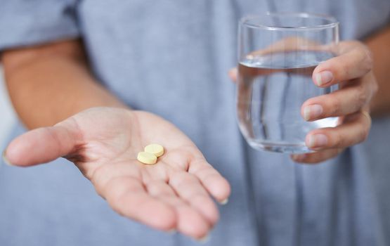 I take these daily. a senior woman holding a glass of water and two tablets.