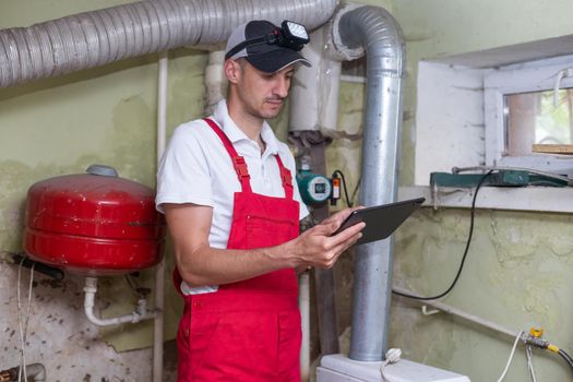The technician checking the heating system in the boiler room with tablet in hand.