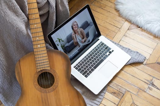 Young woman practicing and learning how to play guitar on laptop computer monitor. Female guitarist watching online tutorial.