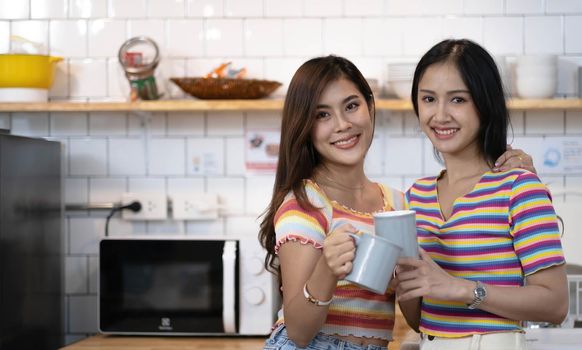 lesbian couple holding coffee mugs in kitchen looking at camera