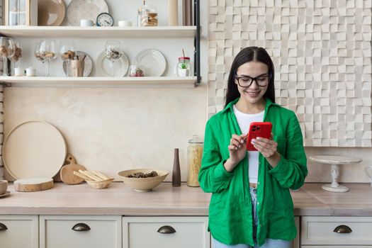 Beautiful woman in glasses and green shirt using red mobile phone at home