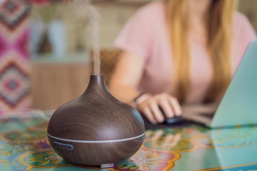 Essential oil diffuser on the table steaming while woman using laptop