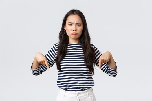Lifestyle, beauty and fashion, people emotions concept. Disappointed upset young asian woman pouting and frowning displeased, pointing fingers down as complaining about product or service