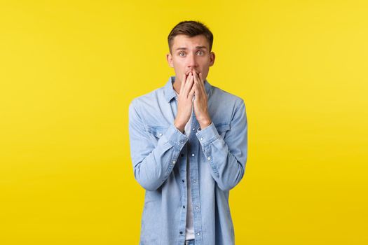 Shocked and worried blond man looking concerned at camera, touching lips and stare anxious at camera, hear about terrible accident, express compassion and empathy, yellow background
