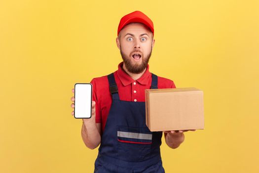 Astonished courier holding cardboard box and smart phone with empty screen.