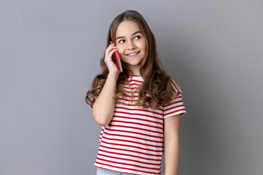 Little girl holding phone near his ear, talking with friends, favorable tariff for calls in roaming.