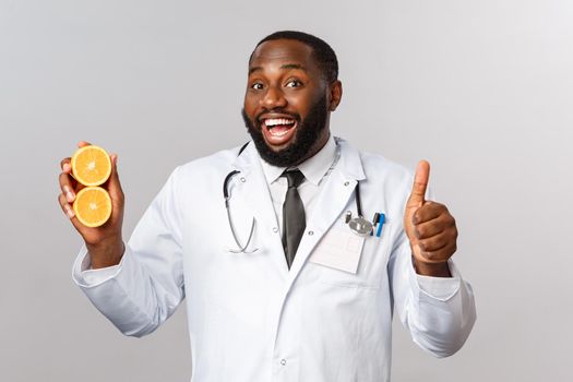 Healthcare, healthy diet and disease concept. Handsome african-american bearded doctor, physician or diatologist recommend eat fruits, showing oranges, avoid junk food, smile and thumb-up