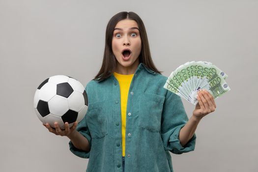 Amazed woman showing soccer ball and hundred euro bills, winning lot of money betting for sport.