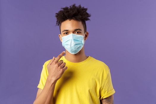 Covid19, healthcare and medicine concept. Young hispanic guy with afro haircut, wear and point at face mask, social-distancing during pandemic, explain friends how to prevent catching disease