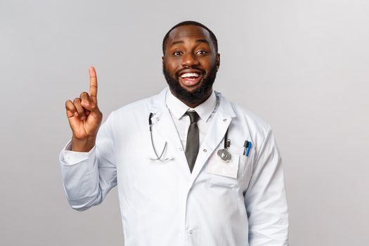 Portrait of cheerful african-american male doctor explain one simple task for patient stay healthy, not getting covid19, make daily check-up in hospical, smiling and showing number one, index finger