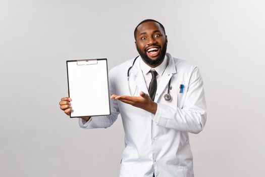 Medicine, covid19, treatment and hospital concept. Annoyed young sarcastic african-american doctor tired of explaining patient or nurse info, pointing at clipboard with irritated expression