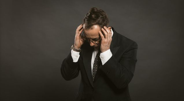 businessman in a depression holds his hands on his head. man in a suit with gray background clasped his head with his hands in a panic. Business problem concept