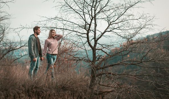 Happy Man and Woman dating in nature. Couple of young people in love stands holding hands while admiring the natural landscape. Adventure and travel concept