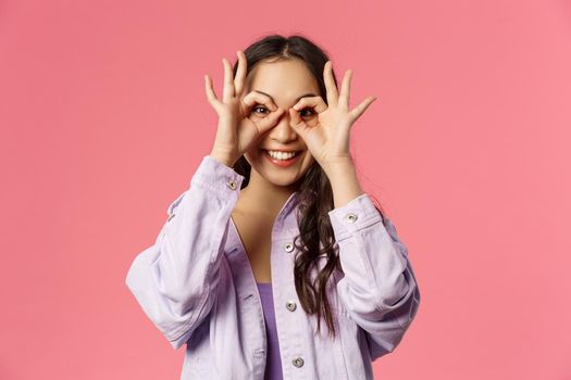 Close-up portrait of charismatic, funny and cute carefree teenage asian girl, making mask with fingers over eyes, smiling and looking camera, having fun, fool around and playing cheerful