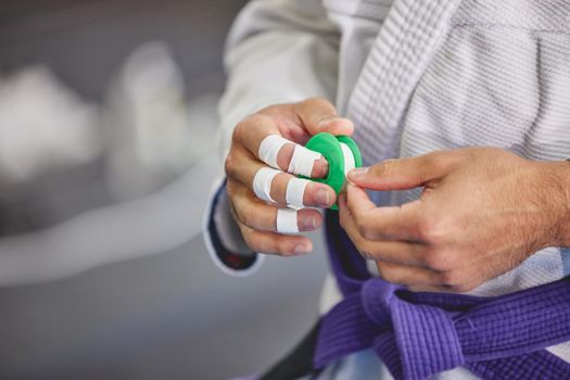 Safety is key. Closeup shot of an unrecognizable young man wrapping his fingers while in full jiu jitsu gi in the gym.