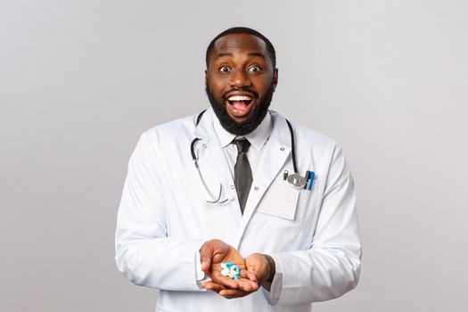 Flu, disease, healthcare and medicine concept. Excited cheerful african-american doctor look amazed, sharing great news, holding new invented medication from influenza or disease, hold pills amused