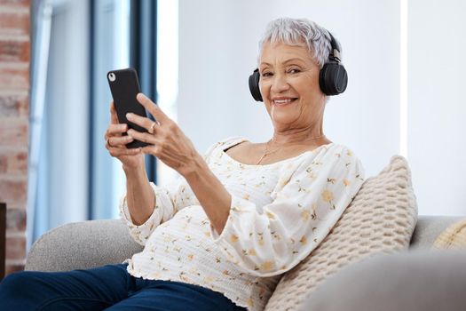 The niftiest little entertainment device. a senior woman using a smartphone and headphones on the sofa at home.