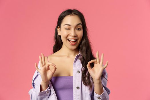 Gotcha, count on me. Close-up portrait of carefree chill and relaxed young girl say no proble, guarantee all be good, show okay signs and wink assuring everything ok, pink background