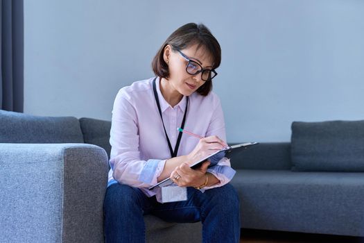 Female psychologist with clipboard working sitting on couch in office