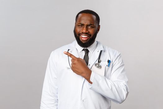 Healthcare, medicine and epidemic concept. Skeptical and judgemental african-american doctor judging people treating virus symptoms with homeopathy, grimace and pointing finger left