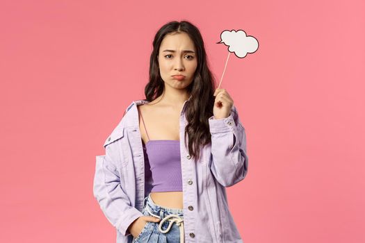 Holidays, lifestyle and people concept. Portrait of gloomy, sulking asian girl dont have any ideas, holding thinking cloud stick and look upset camera as cant figure out plan, pink background