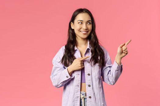 Portrait of curious good-looking asian girl seeing something interesting, peeking and pointing fingers right at promo, look at online courses advertisement, cafe or product promotion
