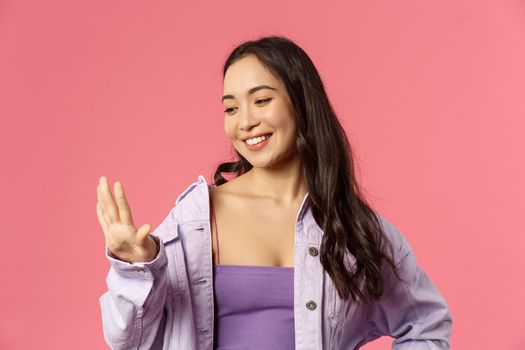 Close-up portrait of pleased good-looking asian girl pleased with great neat manicure, looking at her fingers with smiling satisfied expression, visited nails salon, standing pink background