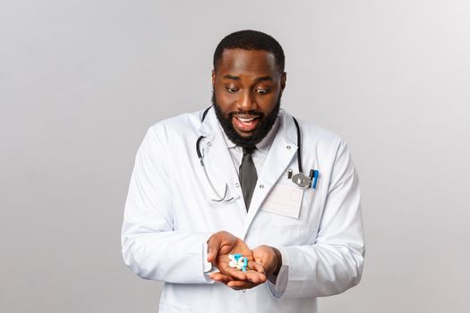 Flu, disease, healthcare and medicine concept. Excited and enthusiastic african-american doctor look astonished and happy at lots of pills in hands, smiling cheerful, have treatment for covid19
