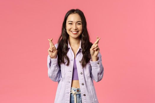 Portrait of excited attractive young korean girl having faith everything be good, keep fingers crossed while making wish, dreaming about desire come true, pink background